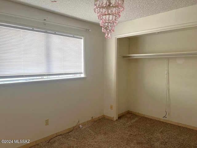 unfurnished bedroom with a chandelier, a textured ceiling, light carpet, and a closet