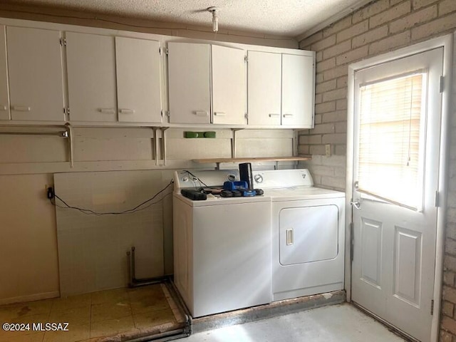 washroom featuring washer and clothes dryer, cabinets, and brick wall