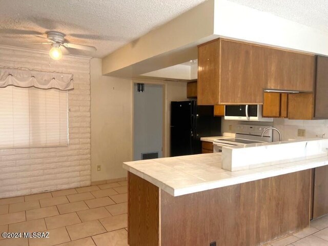 kitchen with black refrigerator, kitchen peninsula, a textured ceiling, ceiling fan, and white electric range