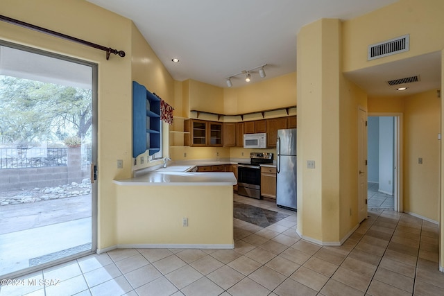 kitchen with appliances with stainless steel finishes, kitchen peninsula, sink, and light tile patterned floors