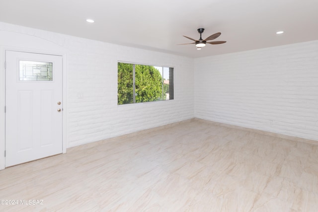 unfurnished room with ceiling fan and brick wall