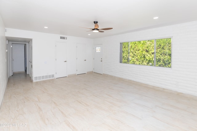 spare room featuring ceiling fan and brick wall