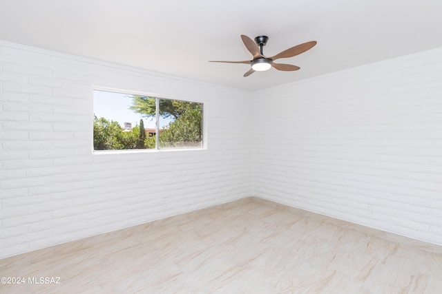 spare room featuring ceiling fan and brick wall