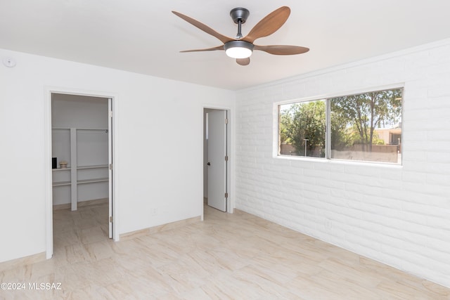 unfurnished bedroom featuring ceiling fan, a walk in closet, a closet, and brick wall