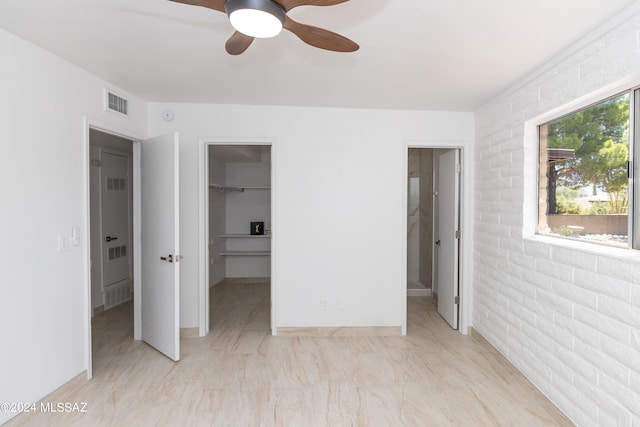 unfurnished bedroom with a spacious closet, a closet, ceiling fan, and brick wall