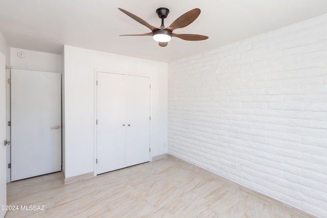 unfurnished bedroom featuring a closet, ceiling fan, and brick wall