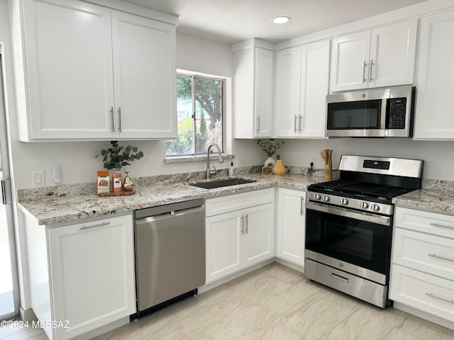 kitchen with light stone countertops, stainless steel appliances, white cabinetry, and sink