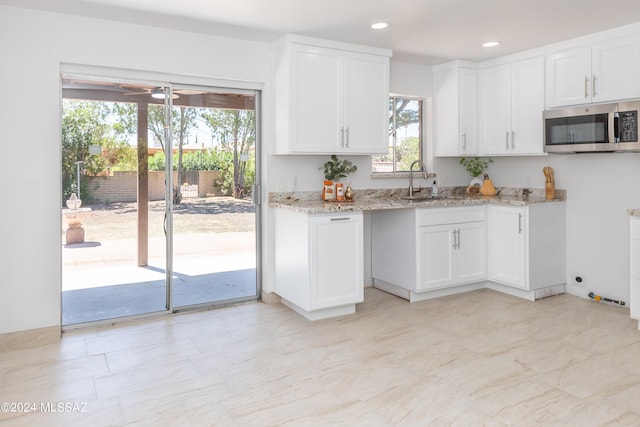 kitchen with sink, white cabinetry, ceiling fan, and light stone counters