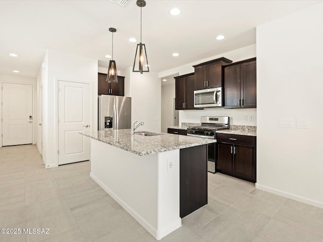 kitchen with a center island with sink, stainless steel appliances, dark brown cabinetry, light stone counters, and pendant lighting