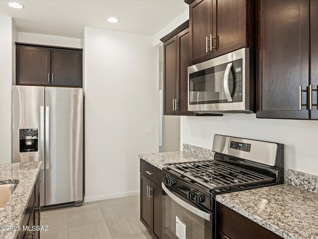 kitchen with dark brown cabinetry, appliances with stainless steel finishes, and light stone countertops