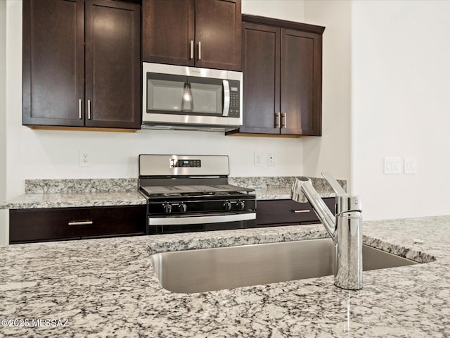 kitchen with sink, dark brown cabinets, light stone countertops, and stainless steel appliances