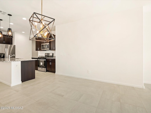 kitchen with appliances with stainless steel finishes, light stone counters, dark brown cabinetry, and decorative light fixtures