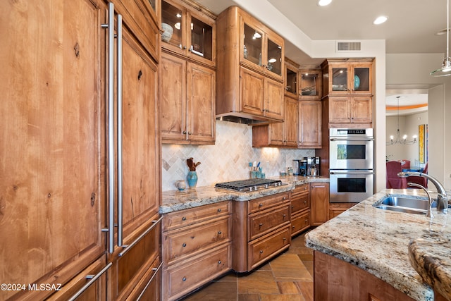 kitchen featuring hanging light fixtures, light stone counters, sink, and stainless steel appliances