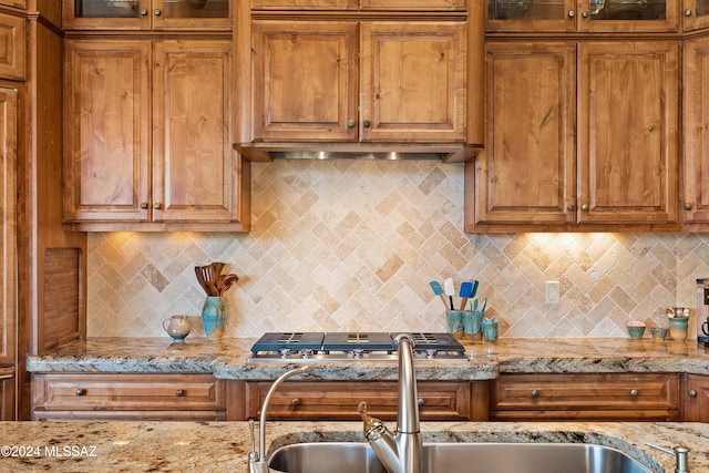 kitchen with stainless steel gas stovetop, light stone countertops, sink, and tasteful backsplash