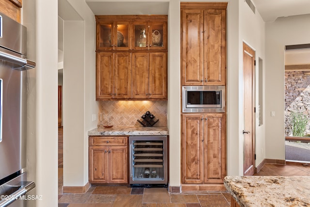 bar with backsplash, light stone countertops, beverage cooler, and appliances with stainless steel finishes