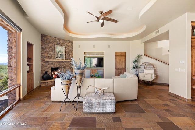 living room featuring ceiling fan, a fireplace, and a tray ceiling