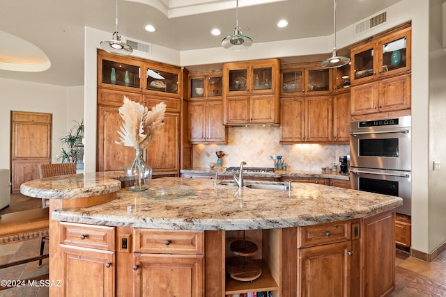 kitchen with sink, a kitchen breakfast bar, double oven, decorative light fixtures, and a kitchen island with sink