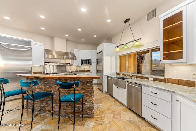 kitchen with a breakfast bar, white cabinets, light stone countertops, decorative light fixtures, and stainless steel appliances