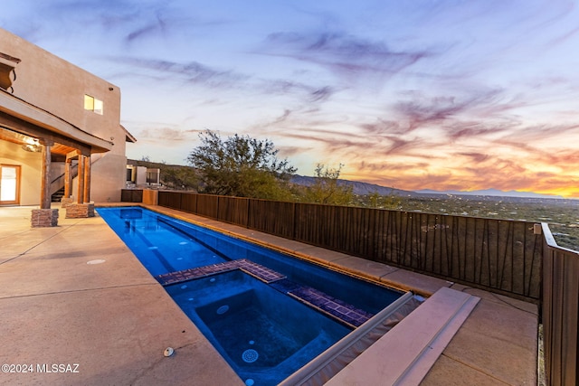 pool at dusk featuring an in ground hot tub, a mountain view, and a patio