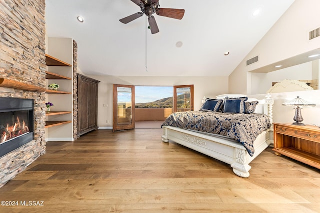 bedroom with a stone fireplace, ceiling fan, hardwood / wood-style floors, and high vaulted ceiling