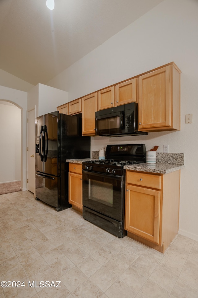 kitchen with light stone countertops, light brown cabinetry, lofted ceiling, and black appliances