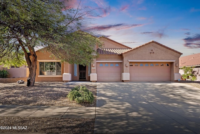 view of front facade featuring a tile roof, an attached garage, concrete driveway, and stucco siding