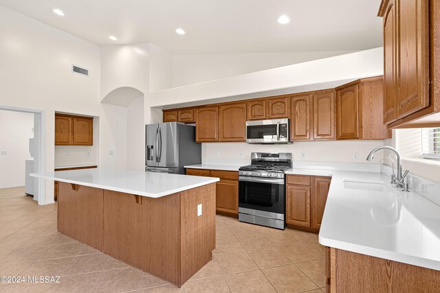 kitchen with stainless steel appliances, a kitchen island, light tile patterned floors, and high vaulted ceiling