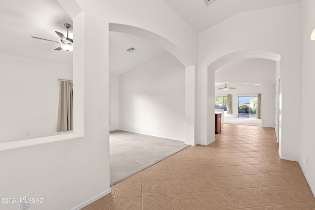 hall featuring carpet, baseboards, lofted ceiling, arched walkways, and tile patterned floors