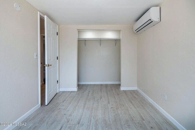 unfurnished bedroom with a wall mounted air conditioner, a closet, and light hardwood / wood-style flooring