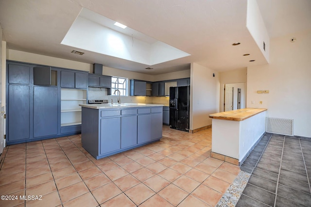 kitchen with light tile patterned floors, sink, black refrigerator with ice dispenser, and a center island