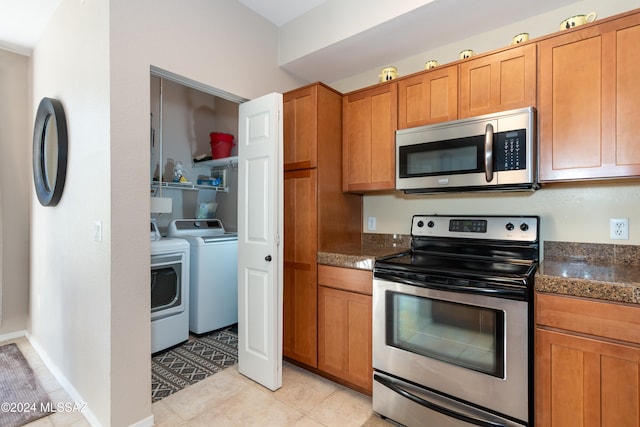 kitchen with appliances with stainless steel finishes, washer and dryer, dark stone counters, and light tile patterned floors