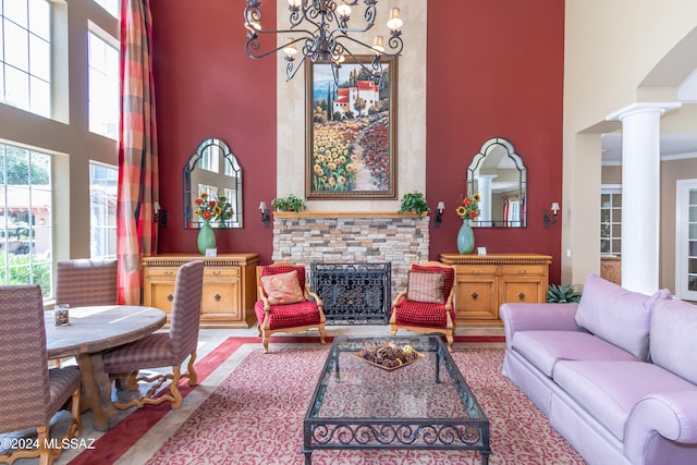 living room featuring a high ceiling, ornate columns, and a stone fireplace