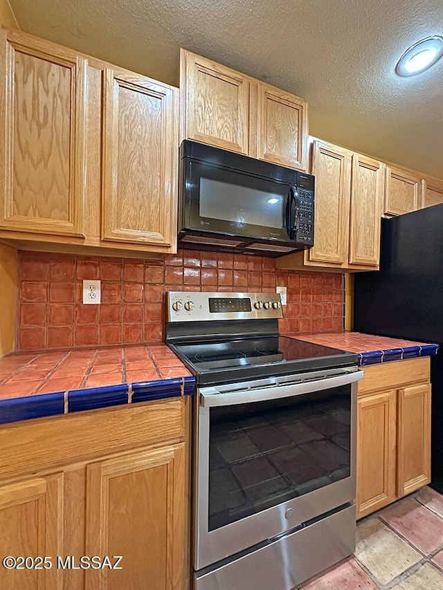 8034 E Shadow Ln, Tucson, AZ 85750 - kitchen featuring black appliances, tile counters, light brown cabinetry, and a textured ceiling