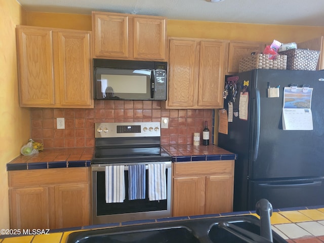 kitchen featuring decorative backsplash, tile counters, and black appliances