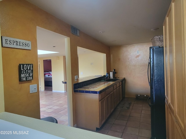 kitchen with sink, tile counters, dark tile patterned floors, and black fridge