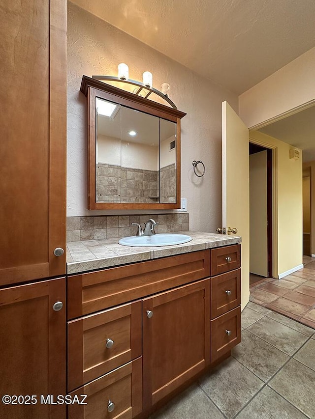8034 E Shadow Ln, Tucson, AZ 85750 - bathroom with a textured wall, vanity, and stone tile flooring