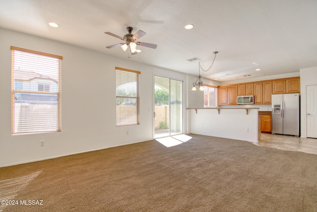 kitchen featuring decorative light fixtures, a kitchen bar, light carpet, ceiling fan with notable chandelier, and appliances with stainless steel finishes