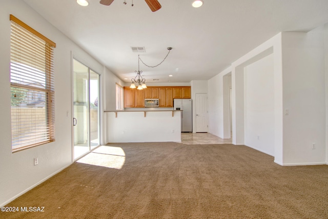 unfurnished living room with light carpet and ceiling fan with notable chandelier