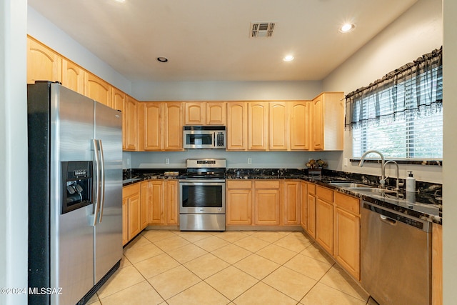 kitchen featuring sink, light tile patterned flooring, dark stone counters, and appliances with stainless steel finishes