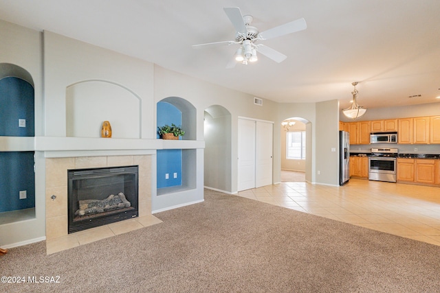 unfurnished living room with ceiling fan, light carpet, and a tile fireplace