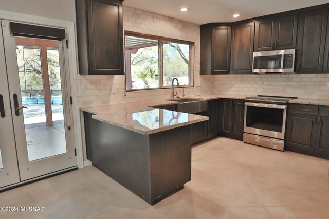 kitchen with dark brown cabinetry, sink, light stone countertops, and appliances with stainless steel finishes