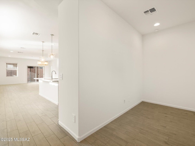 hallway with visible vents, a sink, light wood-style flooring, and baseboards