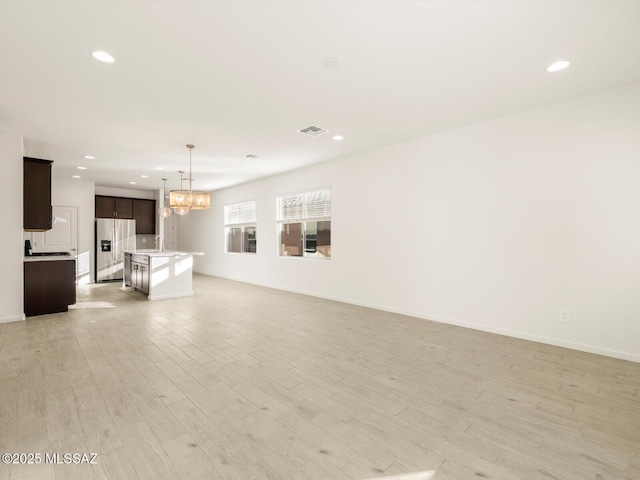 unfurnished living room with light wood-style flooring, recessed lighting, visible vents, baseboards, and an inviting chandelier