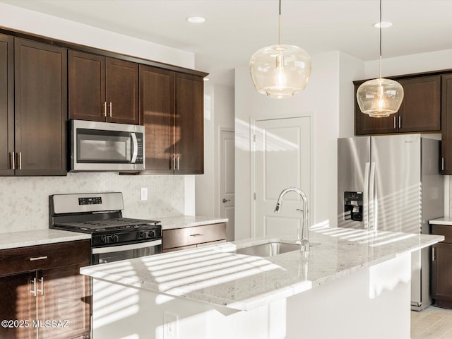 kitchen with dark brown cabinetry, decorative backsplash, light stone counters, appliances with stainless steel finishes, and a sink