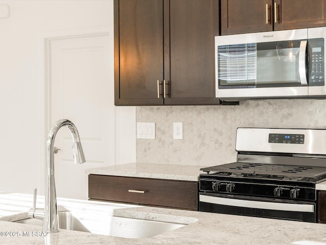 kitchen with dark brown cabinetry, backsplash, stainless steel appliances, and a sink