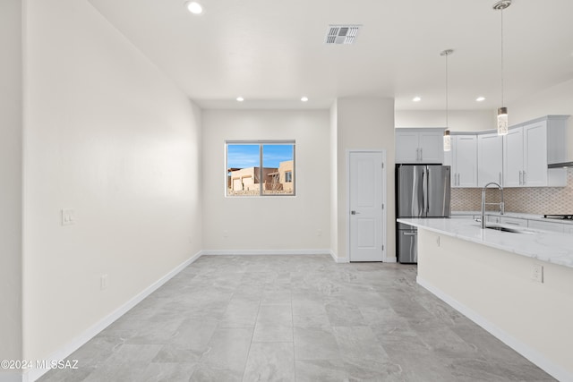 kitchen featuring pendant lighting, sink, stovetop, light stone counters, and stainless steel refrigerator