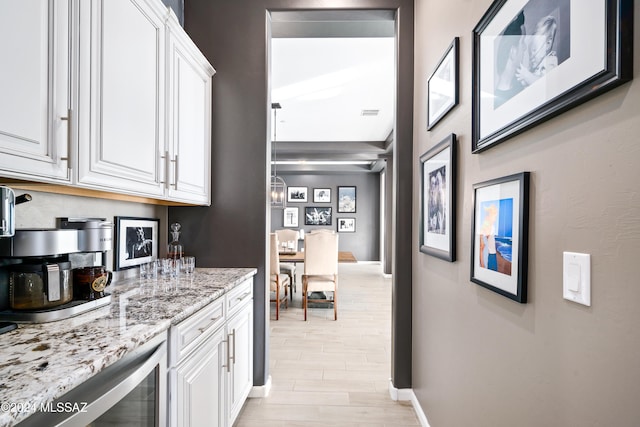 bar with white cabinets, light wood-type flooring, light stone countertops, and beverage cooler