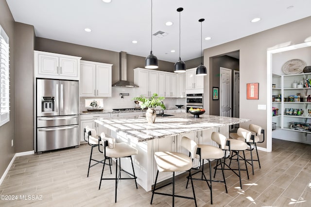 kitchen featuring wall chimney exhaust hood, white cabinetry, stainless steel appliances, and a kitchen island with sink