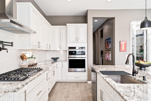 kitchen with stainless steel appliances, sink, wall chimney range hood, white cabinets, and light hardwood / wood-style floors