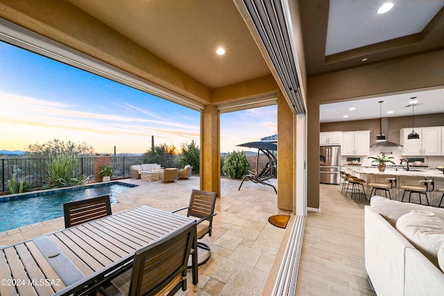 patio terrace at dusk with an outdoor living space, a fenced in pool, and sink